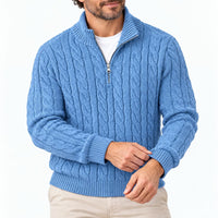 Man in blauwe kabeltrui met halve rits, handen aan de manchet, op witte achtergrond met beige broek. 1