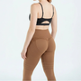 Achteraanzicht van een bruine legging met hoge tailleband en gebogen lijnen over de billen, gedragen met zwarte sporttop. 8
