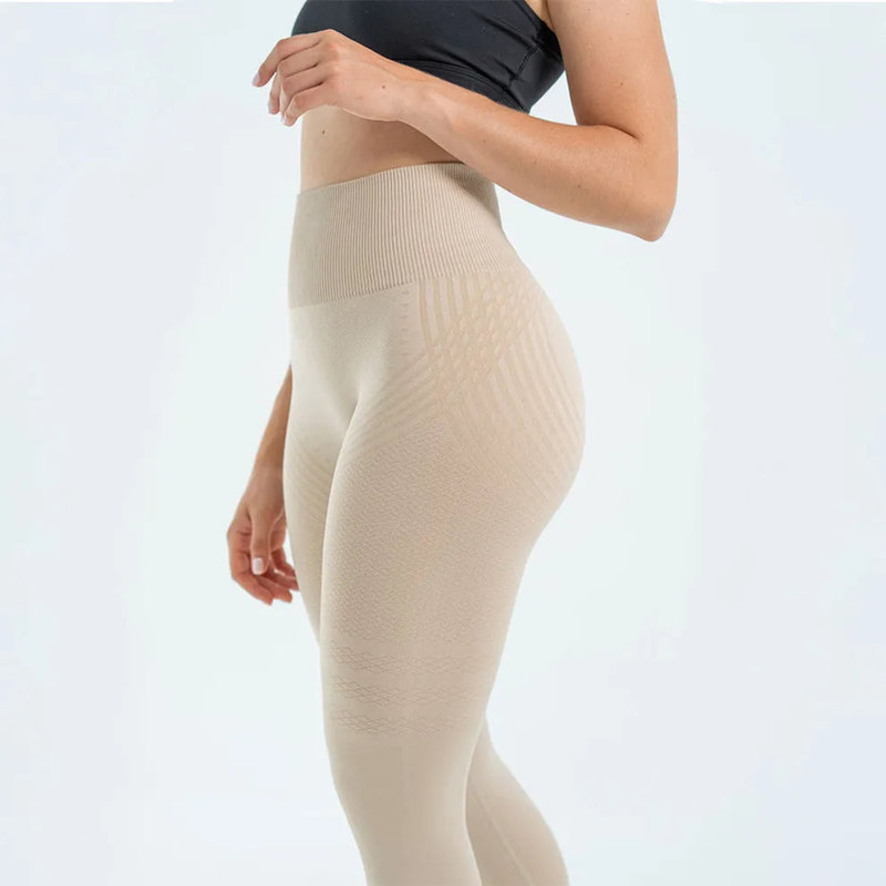 Zijaanzicht van een beige legging met brede geribbelde tailleband en subtiel golvend patroon over de heup en bovenbeen. 2
