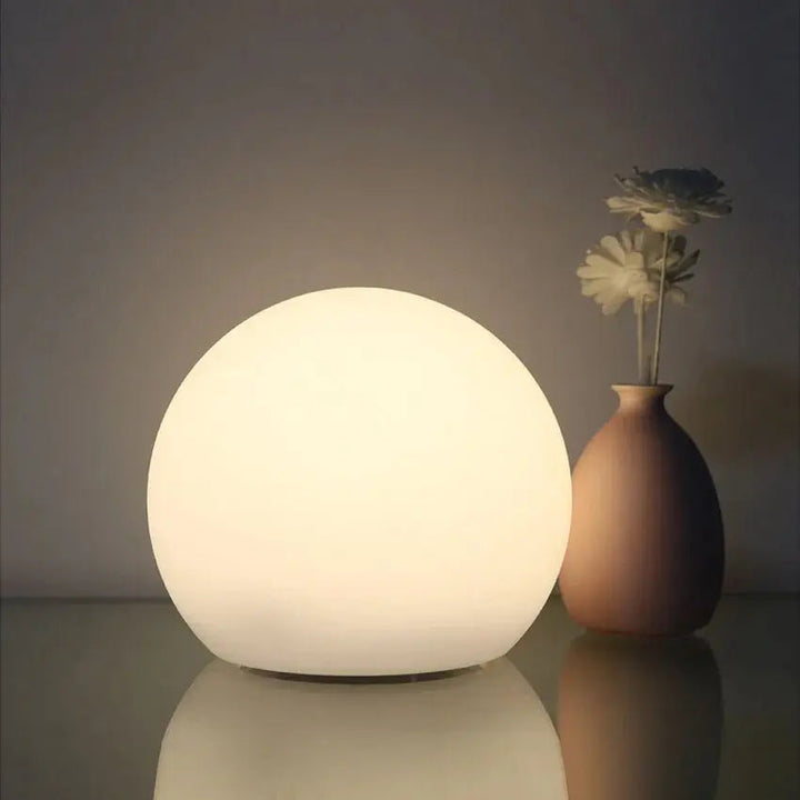 Zacht wit verlichte bollamp op een glanzend oppervlak, naast een bruine vaas met twee bloemen. 2