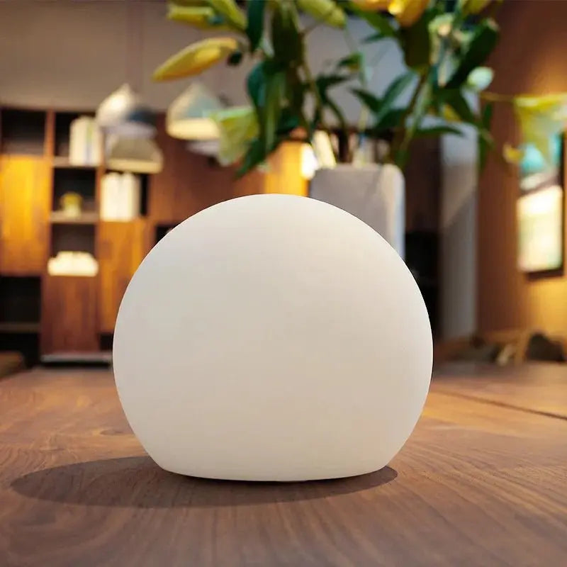 Uitgeschakelde witte bollamp op een houten tafel in een woonkamer met planten en een open kast op de achtergrond. 3