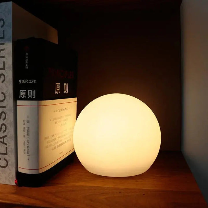 Warm oplichtende bollamp op een plank, tegen een rechtopstaand boek aan, als sfeervolle nachtlamp. 4