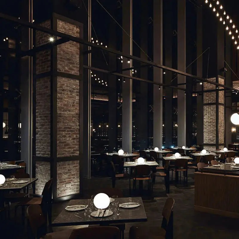 Stijlvol restaurant met bakstenen pilaren, waar op de tafels meerdere lichtgevende bollampen staan als tafelverlichting. 8