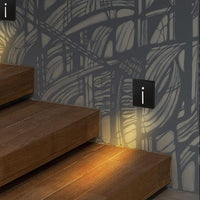 Zwarte wandlampjes met verticale lichtsleuf naast een houten trap, warm licht op de treden en patroonwand 2