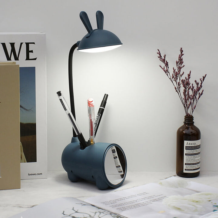 Donkerblauwe lamp met brandend licht op een bureau, met drie pennen in de houder en een spiegel aan de voorkant. 9