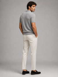 Achterzijde van het grijze poloshirt, model kijkt omgekeerd over zijn schouder, in crèmewitte broek 29