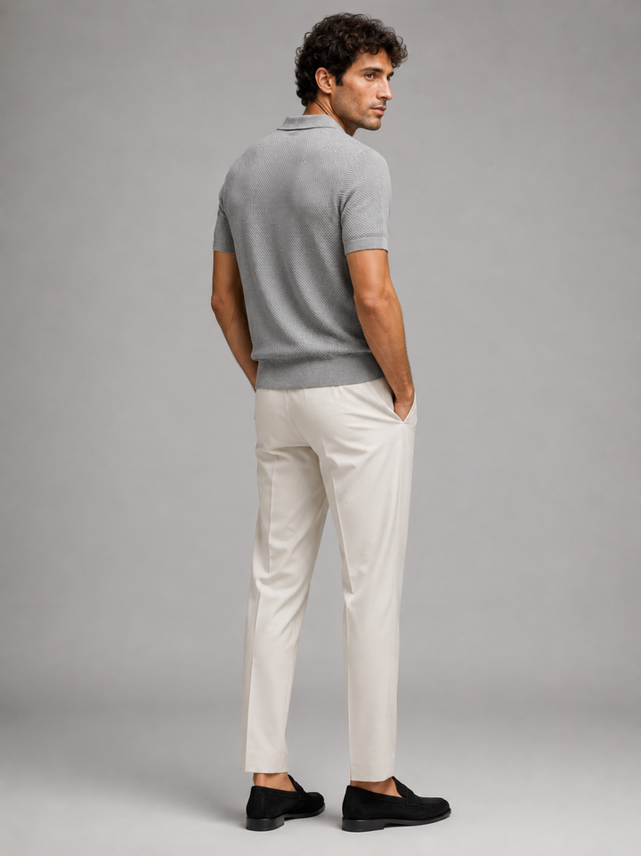 Achterzijde van het grijze poloshirt, model kijkt omgekeerd over zijn schouder, in crèmewitte broek 29