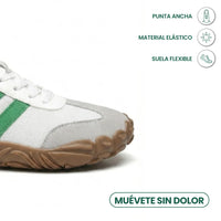 Close-up van de brede neus van een witte sneaker met groene streep en bruine zool, met pictogrammen. 32