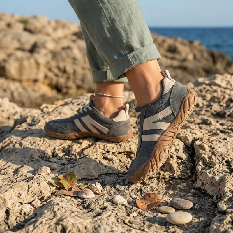 Grijze barefoot schoenen gedragen aan de voeten van een model dat op ruwe rotsen bij de zee loopt. 2