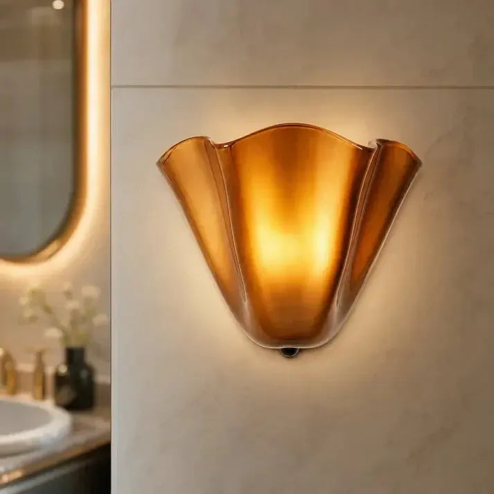 Verlichte amberkleurige wandlamp met golvende rand op een marmerachtige badkamerwand, naast een spiegel met verlichting. 10