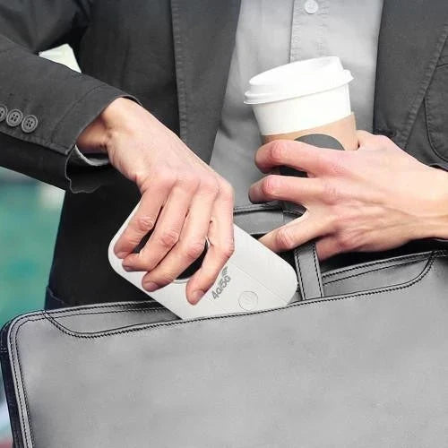 Man in jasje schuift de compacte witte router in een grijze laptoptas, met koffiebeker in de hand 2