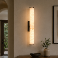 Verlichte marmeren wandlamp in een gang met boogvormige doorgang, boven een tafel met schaal en vaas met takjes. 11