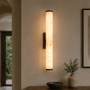 Verlichte marmeren wandlamp in een gang met boogvormige doorgang, boven een tafel met schaal en vaas met takjes. 11