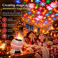 Moeder en twee kinderen in kerstpyjama's kijken onder een deken lachend naar de feestelijke projectie, met de projector op tafel ervoor. 2