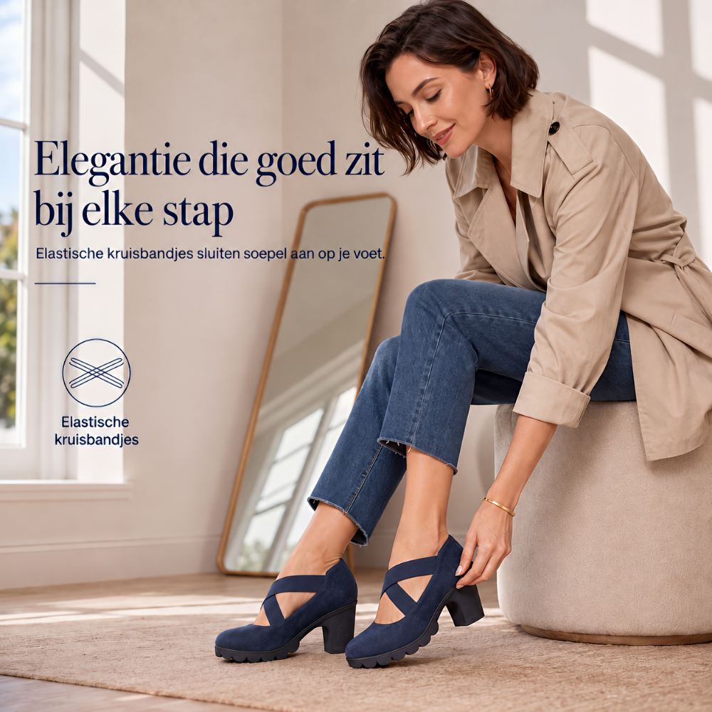 Vrouw in beige jas zit op een poef en trekt de marineblauwe schoen met gekruiste bandjes aan. 4