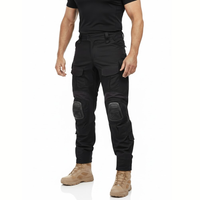 Man in zwart shirt en beige laarzen draagt de zwarte cargobroek met kniekappen, schuin van voren gezien. 2