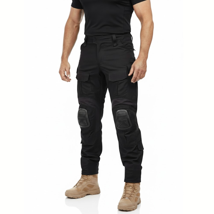 Man in zwart shirt en beige laarzen draagt de zwarte cargobroek met kniekappen, schuin van voren gezien. 2