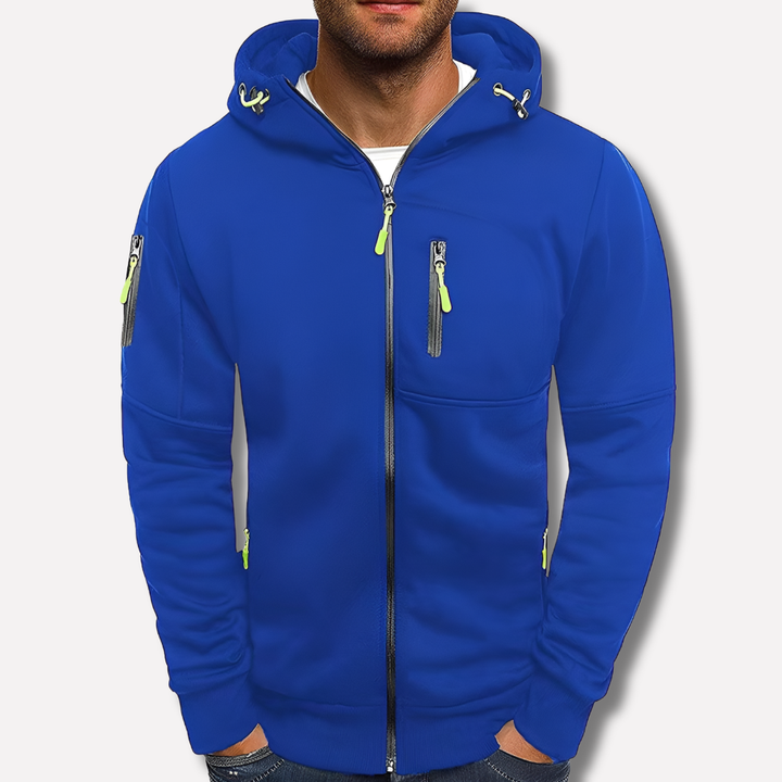 Koningsblauwe hoodie met capuchon en limoengroene ritstrekkers op een effen lichte achtergrond, gedragen door een man met handen in de zakken. 2