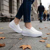 Model draagt witte instapschoenen met blauwe spijkerbroek op een stoep met gevallen bladeren 11