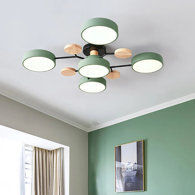 Groene plafondlamp met vier ronde kappen en houten schijfjes aan zwarte armen, aan het plafond van een kamer met groene muur en lijst. 4