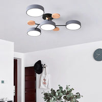 Grijze plafondlamp met vier ronde kappen en houten schijfjes aan zwarte armen, in een witte hal met kapstok, tas en klok. 5