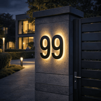 Verlicht zwart huisnummer 99 op een stenen pilaar bij de poort, in een avondsfeer met een woning en tuinverlichting. 2