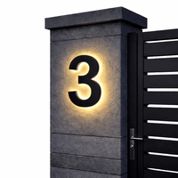 Zwart huisnummer 3 met gloeiende achtergrondverlichting op een grijze stenen pilaar naast een zwarte poort. 9