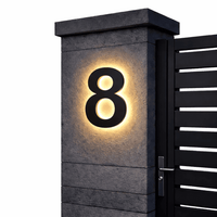Zwart huisnummer 8 met warme achtergrondverlichting op een grijze stenen pilaar naast een zwarte poort, op witte achtergrond. 11