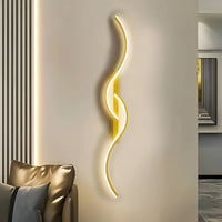 Verlichte gouden golvende wandlamp naast een leren bank in een woonkamer met gestreepte wand 1