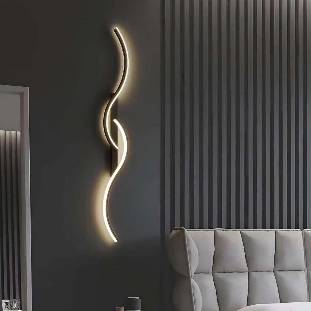 Zwarte golvende wandlamp tegen een donkergrijze wand, naast een grijze gestoffeerde bank 6