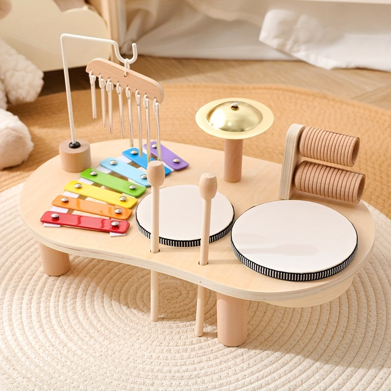 Houten muziektafel met regenboogxylofoon, windgong, bekken, twee trommels en houten rammelaars op een gevlochten vloerkleed, schuin van voren gezien. 1