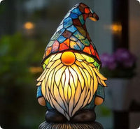 Tuinkabouter met blauwe mozaïekmuts en lange lichtgevende baard, gefotografeerd bij een raam met planten. 13