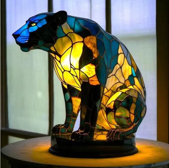 Zittende panter in blauw, groen en geel glas-in-loodmozaïek op een ronde voet, voor een raam. 16