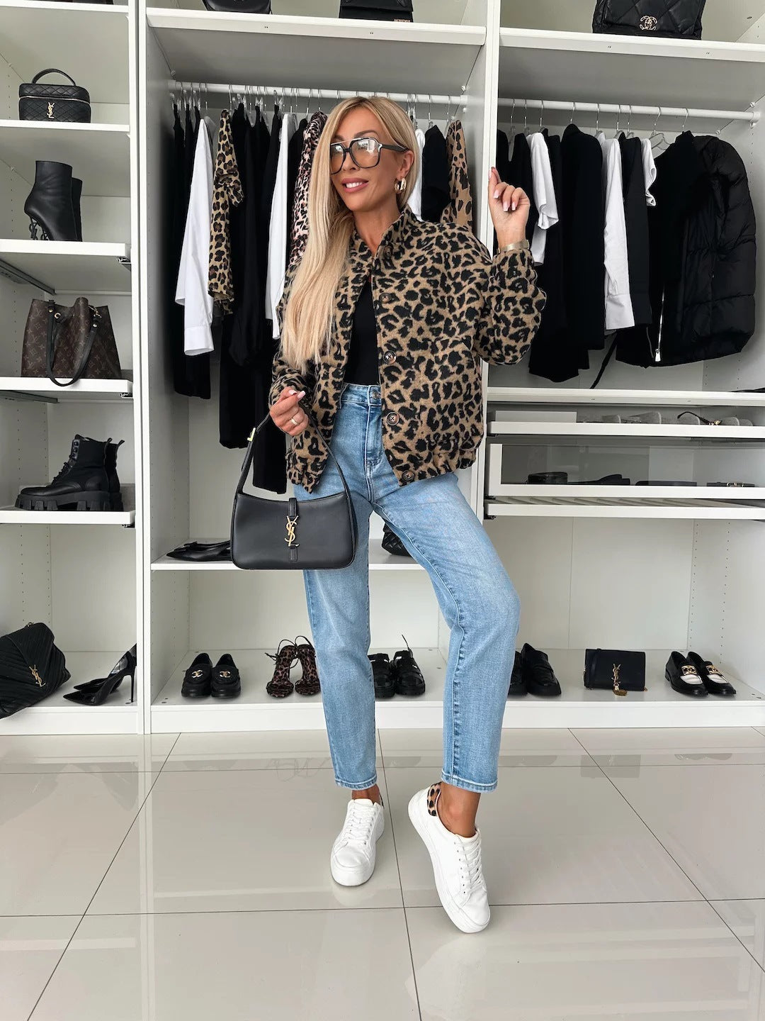 Model in volledige outfit: jasje met luipaardprint, zwarte top, lichtblauwe jeans, witte sneakers en een zwarte handtas in een inloopkast. 5