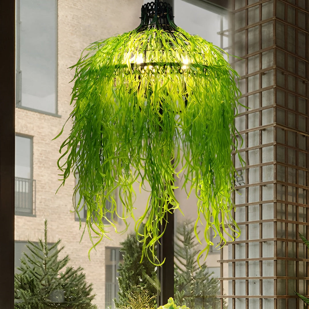 Verlichte kroonluchter behangen met lange, slierterige groene kunstplanten, hangend bij een raam met uitzicht op een stenen 2