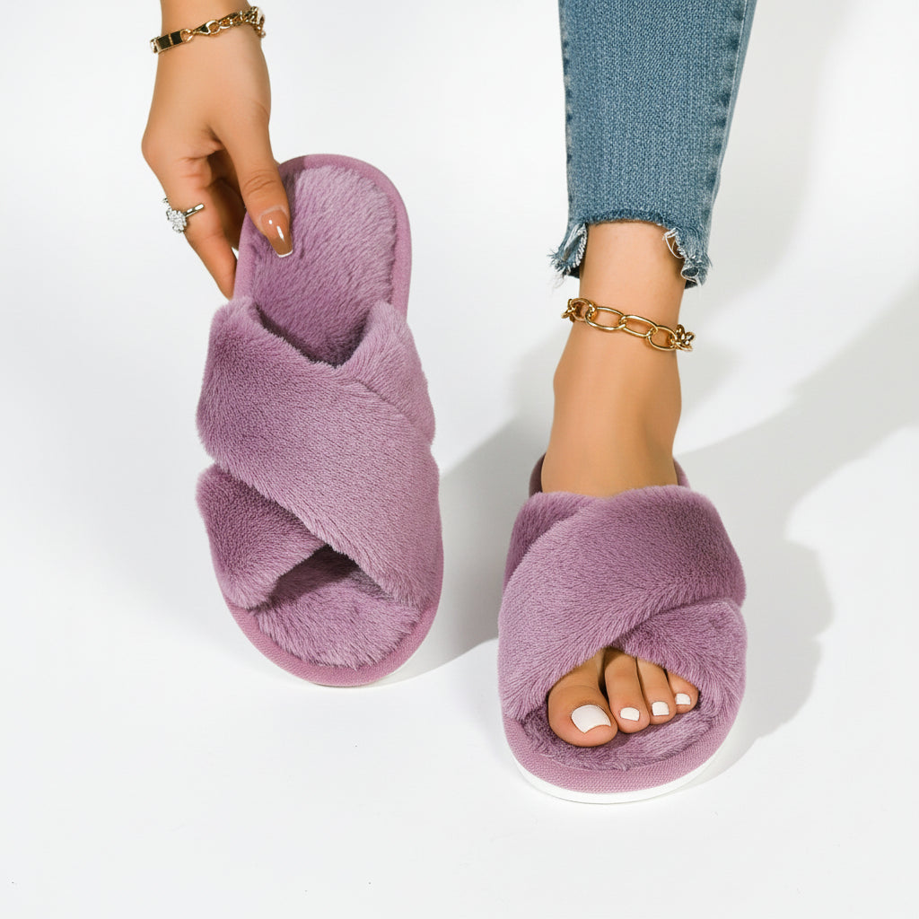 Paarse pluche slippers met gekruiste banden; het model houdt er één omhoog en draagt de andere bij een spijkerbroek. 8
