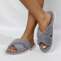 Grijze pluche slippers met gekruiste banden en witte zool, gedragen door een model met de voeten gekruist. 5
