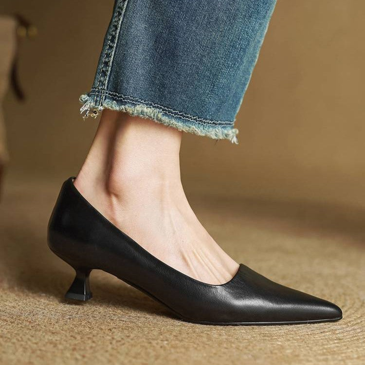 Zwarte pump aan een voet, zijaanzicht met de taps toelopende lage hak en een rafelige jeanspijp 14