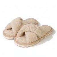 Paar beige pluche slippers met gekruiste banden, schuin van voren gefotografeerd op een witte achtergrond, zonder model. 1