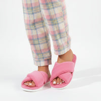 Roze pluche slippers met gekruiste banden gedragen door een model in een pyjamabroek met pastelkleurige ruiten. 2