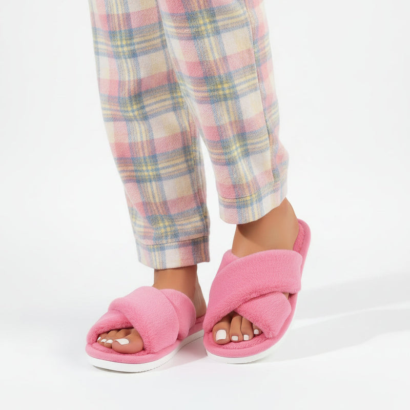 Roze pluche slippers met gekruiste banden gedragen door een model in een pyjamabroek met pastelkleurige ruiten. 2