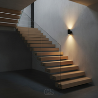 Zwart wandlampje naast een zwevende houten trap met glazen balustrade, dat de muur en treden met warm licht verlicht. 4