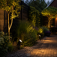Meerdere tuinspots verlichten in de schemering borders met siergras en bomen langs een klinkerpad en een terras. 4