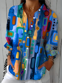 Close-upvoorkant van de blauwe blouse met kleurrijk abstract patroon, witte knopen en V-hals, gedragen door een model. 6