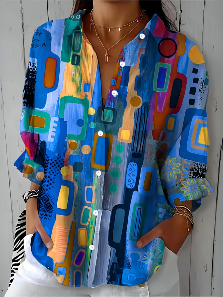 Close-upvoorkant van de blauwe blouse met kleurrijk abstract patroon, witte knopen en V-hals, gedragen door een model. 6
