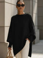Model draagt de oversized trui in zwart met witte broek, zonnebril en beige tas. 6