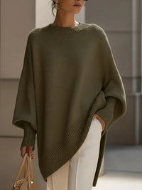 Model draagt de oversized trui in olijfgroen met witte broek en een beige tas in de hand. 7