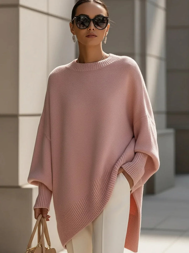 Model draagt de oversized trui in roze met witte broek, zonnebril en beige tas. 11