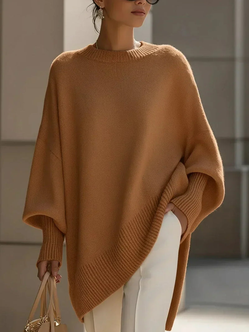 Model draagt de oversized trui in kameelbruin met witte broek en een beige tas in de hand. 12