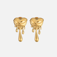 Voorkant van een paar gouden hartvormige oorstekers met druipende druppels, op een lichtgrijze achtergrond. 1